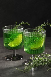 Photo of Glasses of homemade refreshing tarragon drink and sprigs on grey table