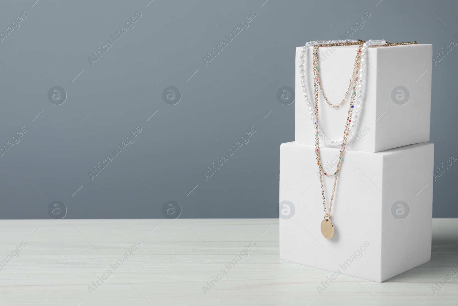 Photo of Stylish presentation of necklaces on podiums on white wooden table, space for text