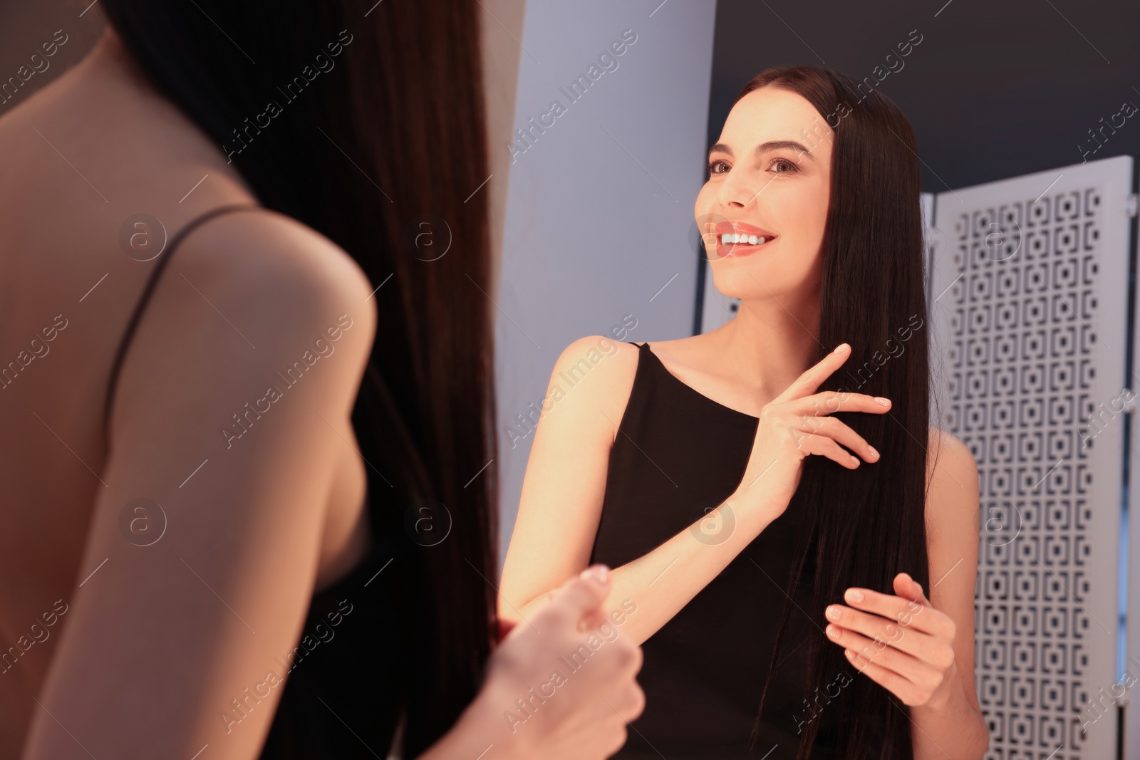 Photo of Beautiful young woman in elegant dress near mirror indoors