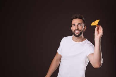 Handsome man playing with paper plane on brown background. Space for text