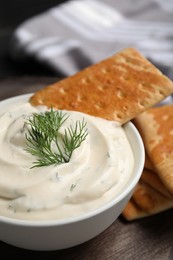 Photo of Tasty creamy dill sauce with cracker in bowl on black wooden table, closeup