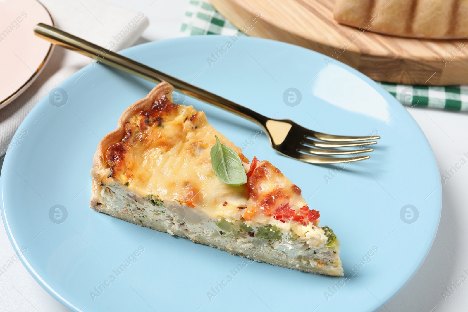 Photo of Piece of tasty quiche with chicken, cheese, basil and vegetables on white table, closeup