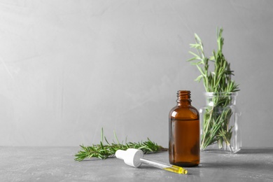 Photo of Bottle and pipette with fresh rosemary oil on table