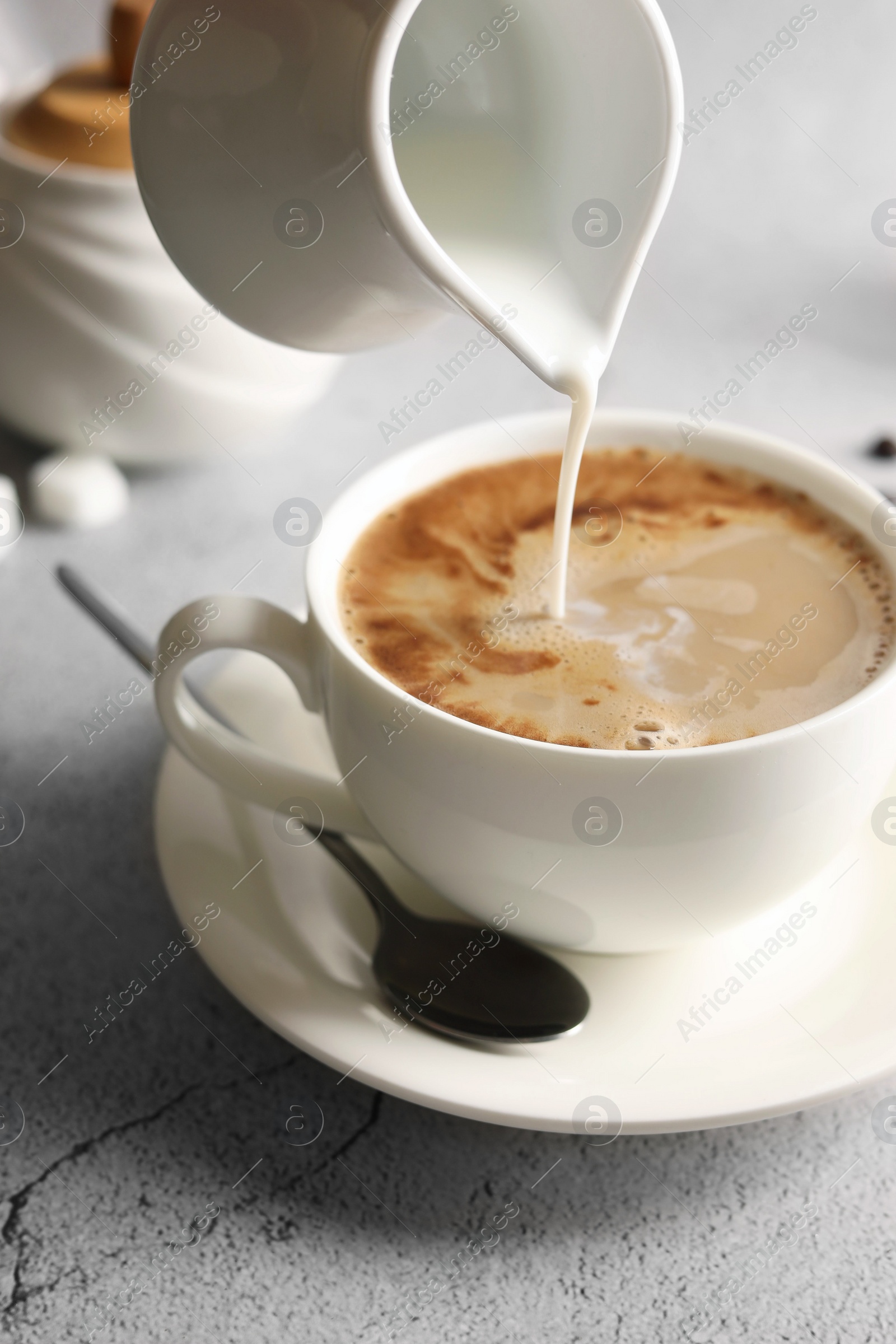 Photo of Pouring milk into cup with coffee on light grey textured table, closeup