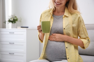 Beautiful pregnant woman drinking tea at home, closeup