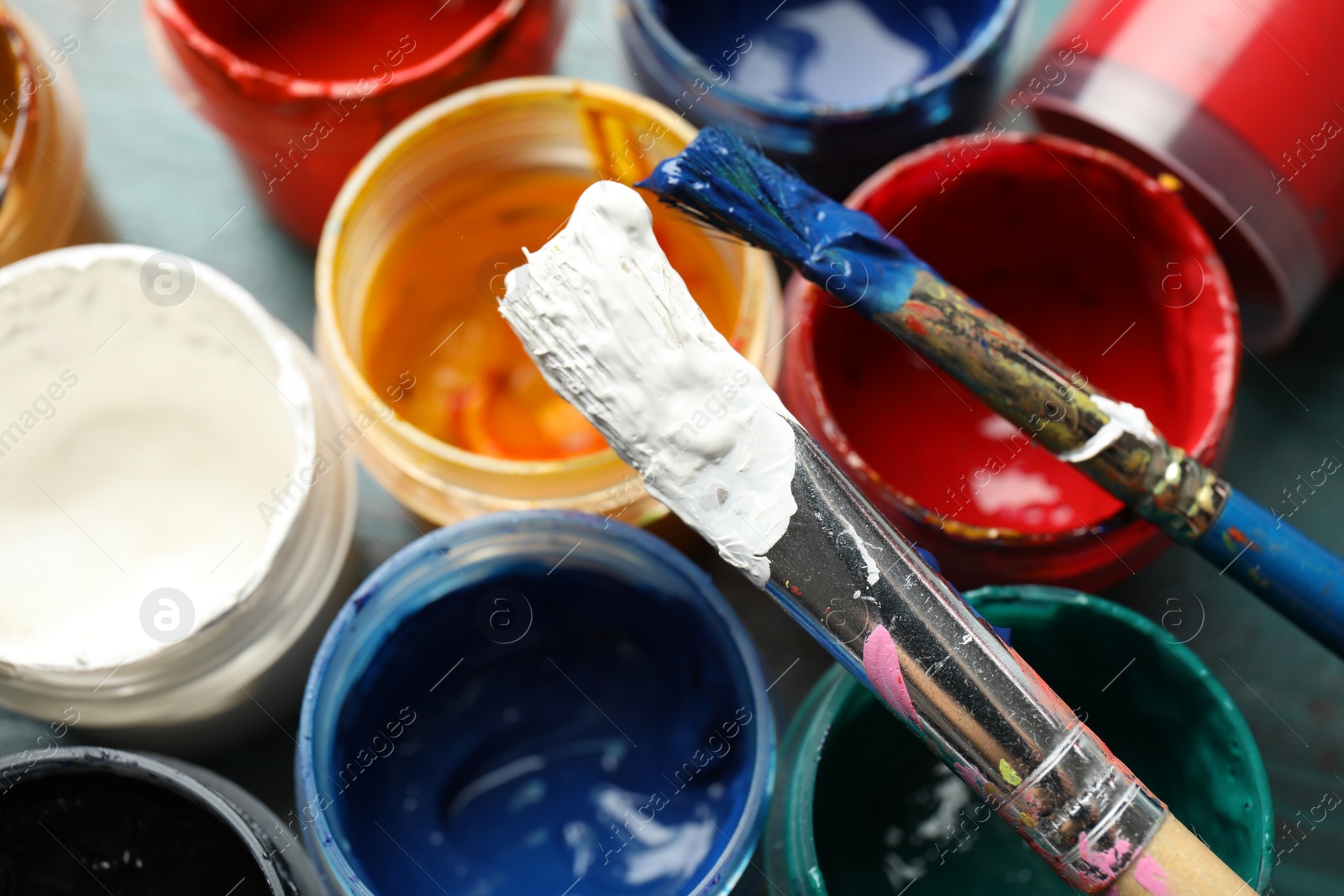 Photo of Jars with color paints and brushes on table, closeup