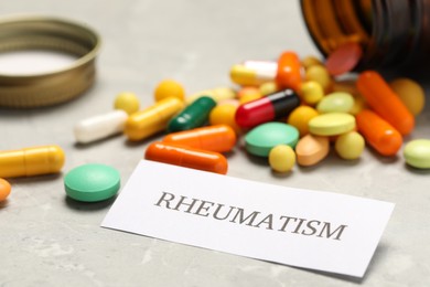 Photo of Card with word Rheumatism and pills on light gray table, closeup
