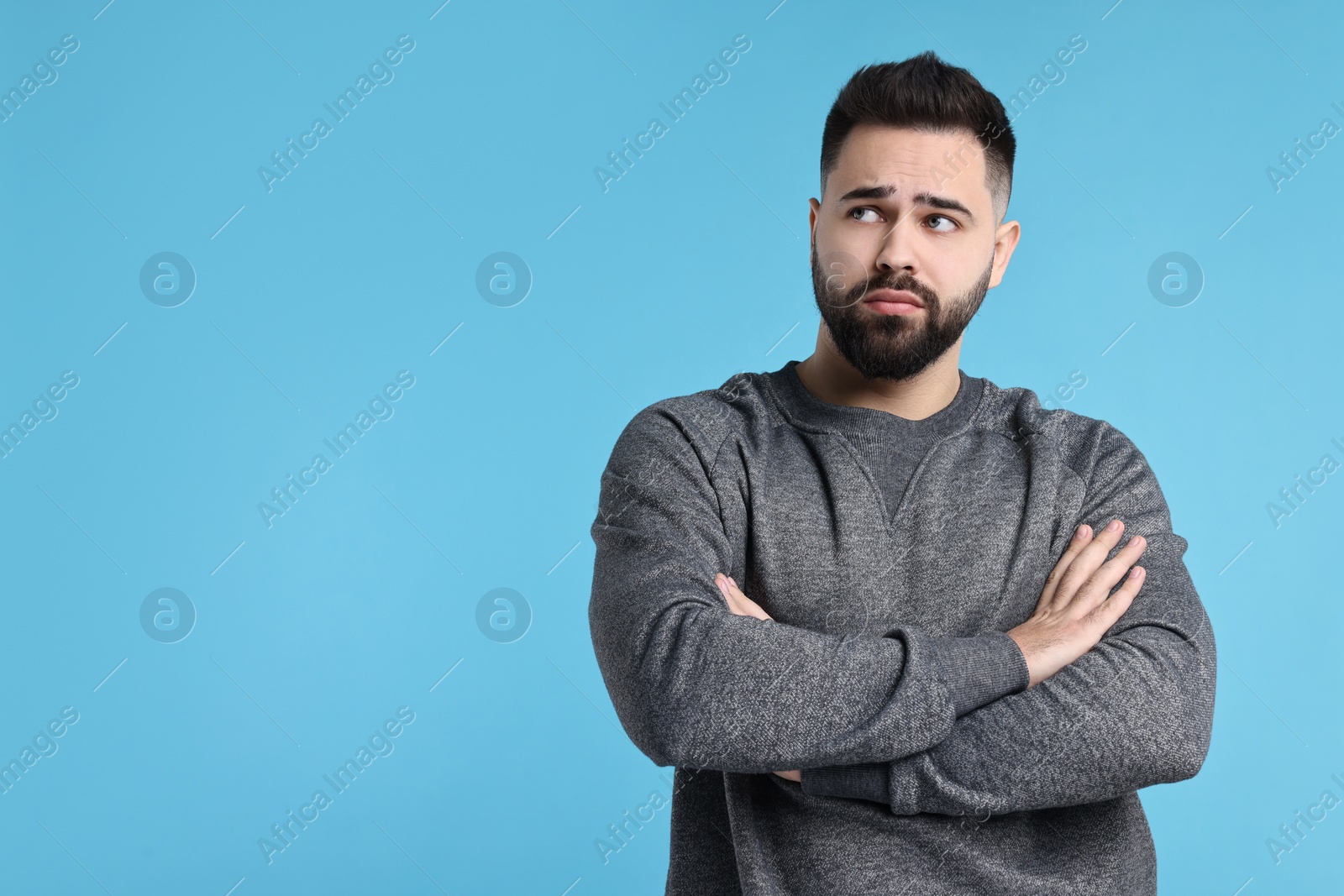 Photo of Portrait of sad man with crossed arms on light blue background, space for text