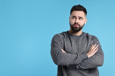 Portrait of sad man with crossed arms on light blue background, space for text