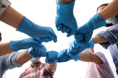 People in blue medical gloves joining fists on light background, low angle view