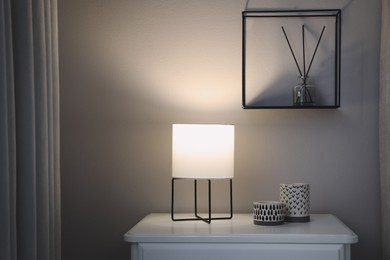 Stylish lamp and candles on white nightstand in room