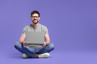 Happy man with laptop on lilac background, space for text