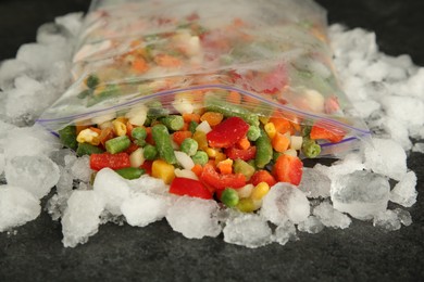 Zip bag with different frozen vegetables and ice on grey table, closeup