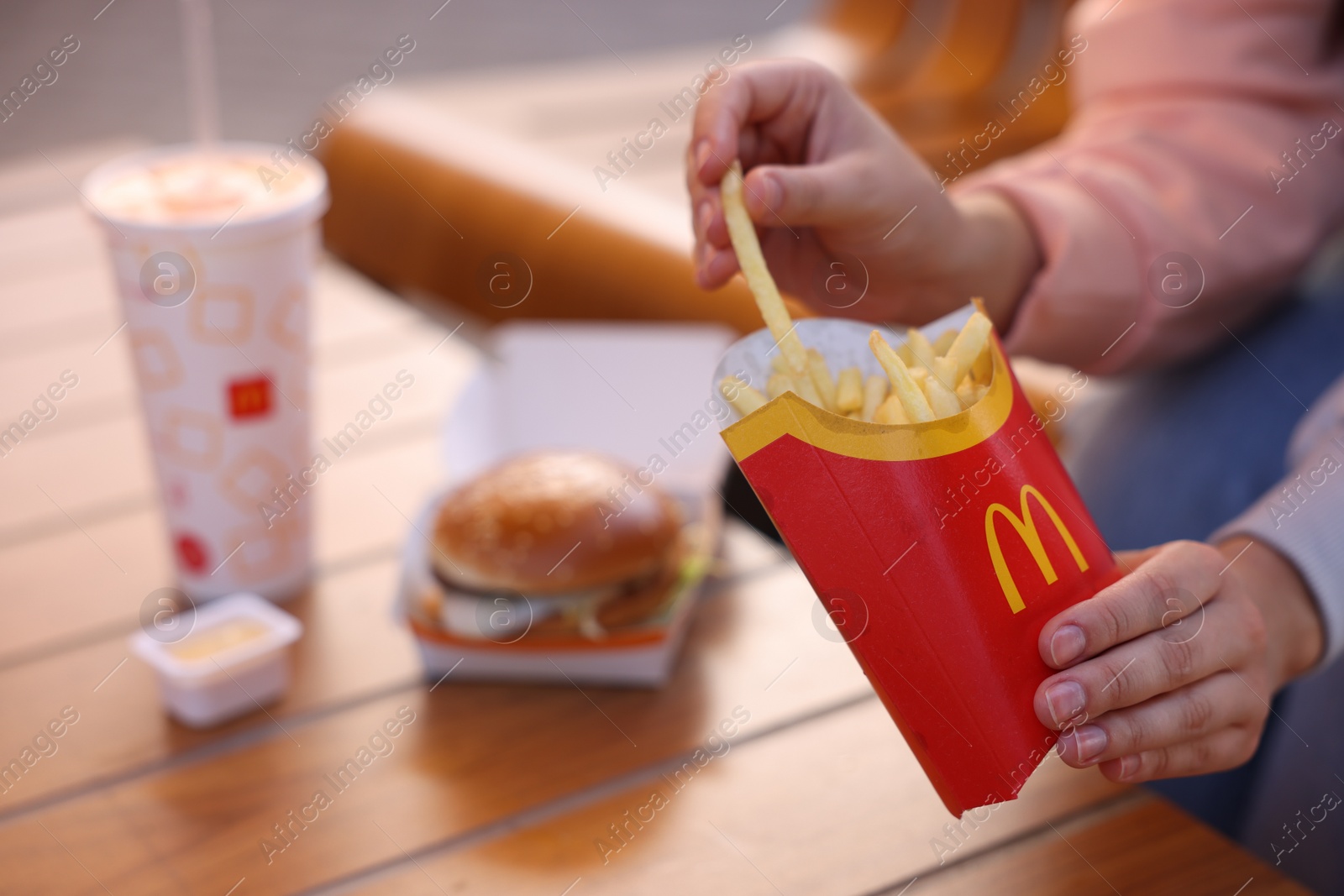 Photo of Lviv, Ukraine - September 26, 2023: Woman eating McDonald's menu at wooden table outdoors, closeup