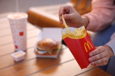 Photo of Lviv, Ukraine - September 26, 2023: Woman eating McDonald's menu at wooden table outdoors, closeup