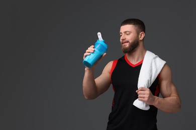 Young man with muscular body holding shaker of protein and towel on grey background, space for text