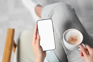 Photo of Woman with smartphone and cup of coffee indoors, closeup. Space for text