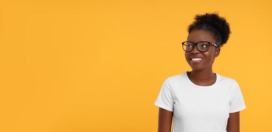 Photo of Portrait of happy young woman in eyeglasses on orange background. Space for text