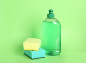 Photo of Bottle of detergent and sponges on green background