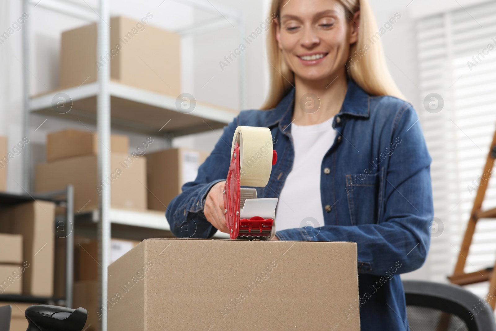 Photo of Seller taping parcel in office, selective focus. Online store