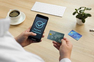 Man successfully made payment using online banking application on smartphone at wooden table, closeup