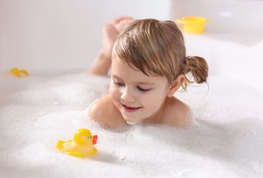 Photo of Smiling girl bathing with toy duck in tub