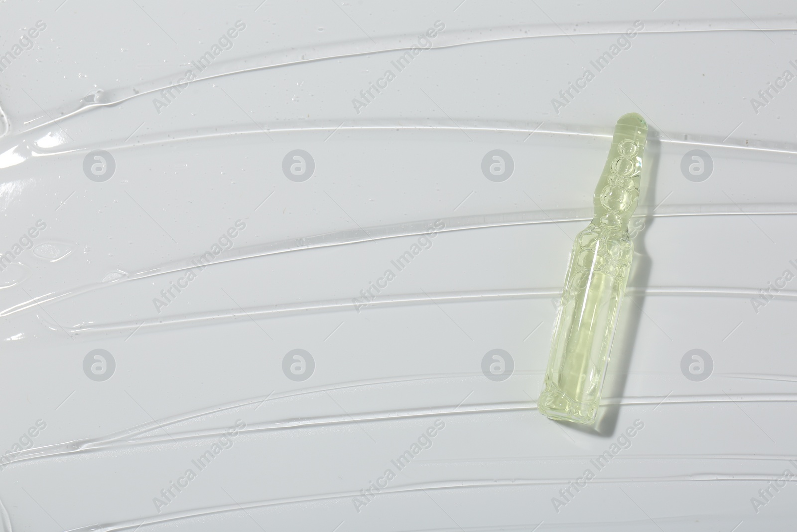 Photo of Skincare ampoule on white surface covered with gel, top view. Space for text