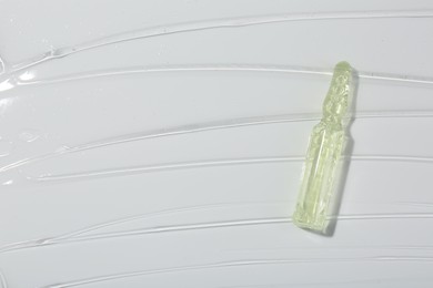 Photo of Skincare ampoule on white surface covered with gel, top view. Space for text