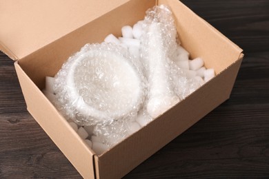Photo of Mortar and pestle with bubble wrap in cardboard box on dark wooden table