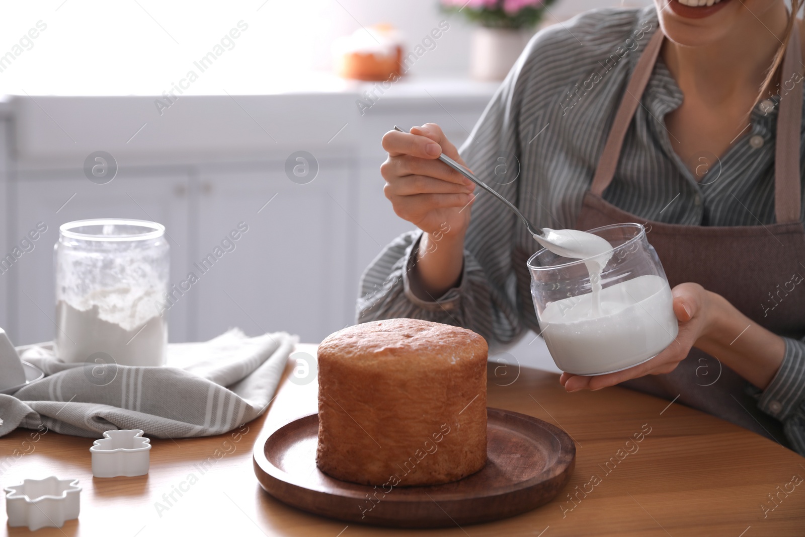 Photo of Young woman decorating traditional Easter cake with glaze in kitchen, closeup. Space for text