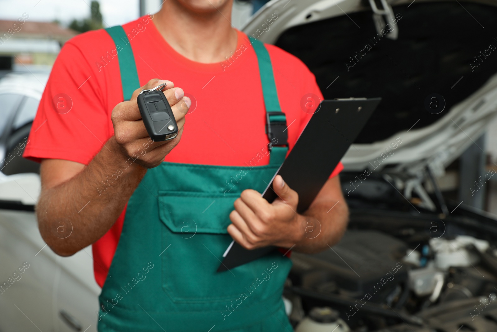 Photo of Mechanic with clipboard and car key at automobile repair shop, closeup