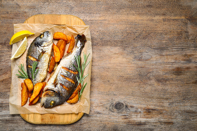 Photo of Delicious roasted fish and potatoes on wooden table, flat lay. Space for text