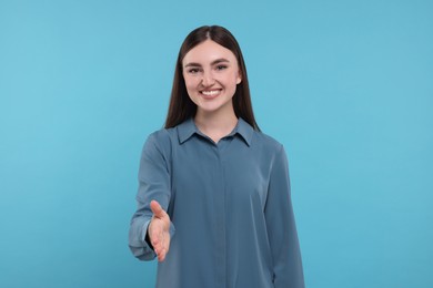 Photo of Smiling woman welcoming and offering handshake on light blue background