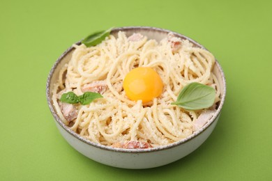 Photo of Bowl of tasty pasta Carbonara with basil leaves on light green background