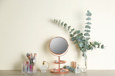 Photo of Mirror with jewelry and makeup products on wooden table near light wall
