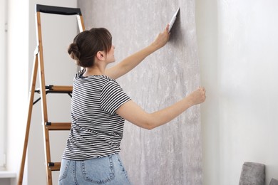 Photo of Woman smoothing stylish gray wallpaper in room