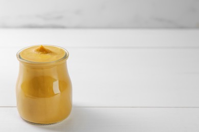 Photo of Tasty mustard sauce in glass jar on white wooden table, space for text