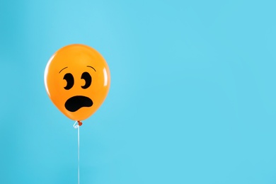 Photo of Orange balloon with drawing of scared face on blue background, space for text. Halloween party