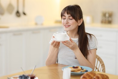 Smiling woman drinking coffee at breakfast indoors. Space for text