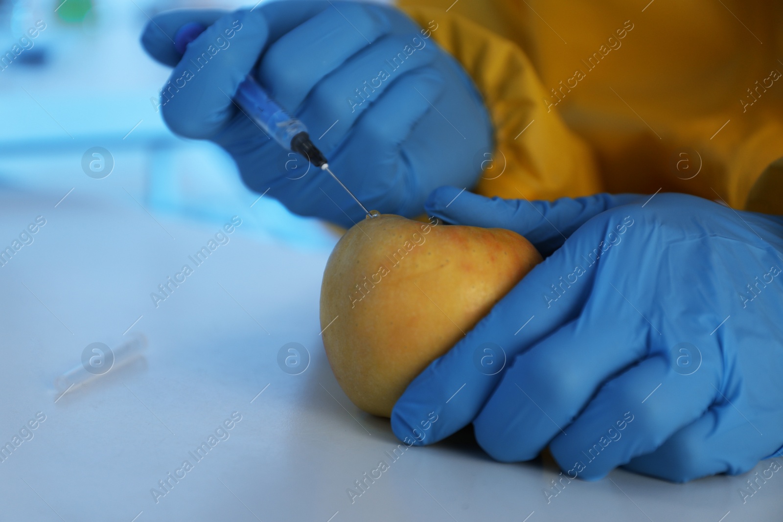 Photo of Scientist in chemical protective suit injecting apple at table, closeup