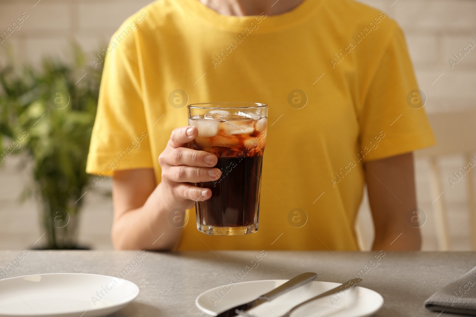 Photo of Woman holding glass of cola with ice at table, closeup