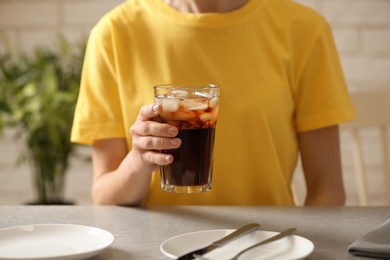 Photo of Woman holding glass of cola with ice at table, closeup