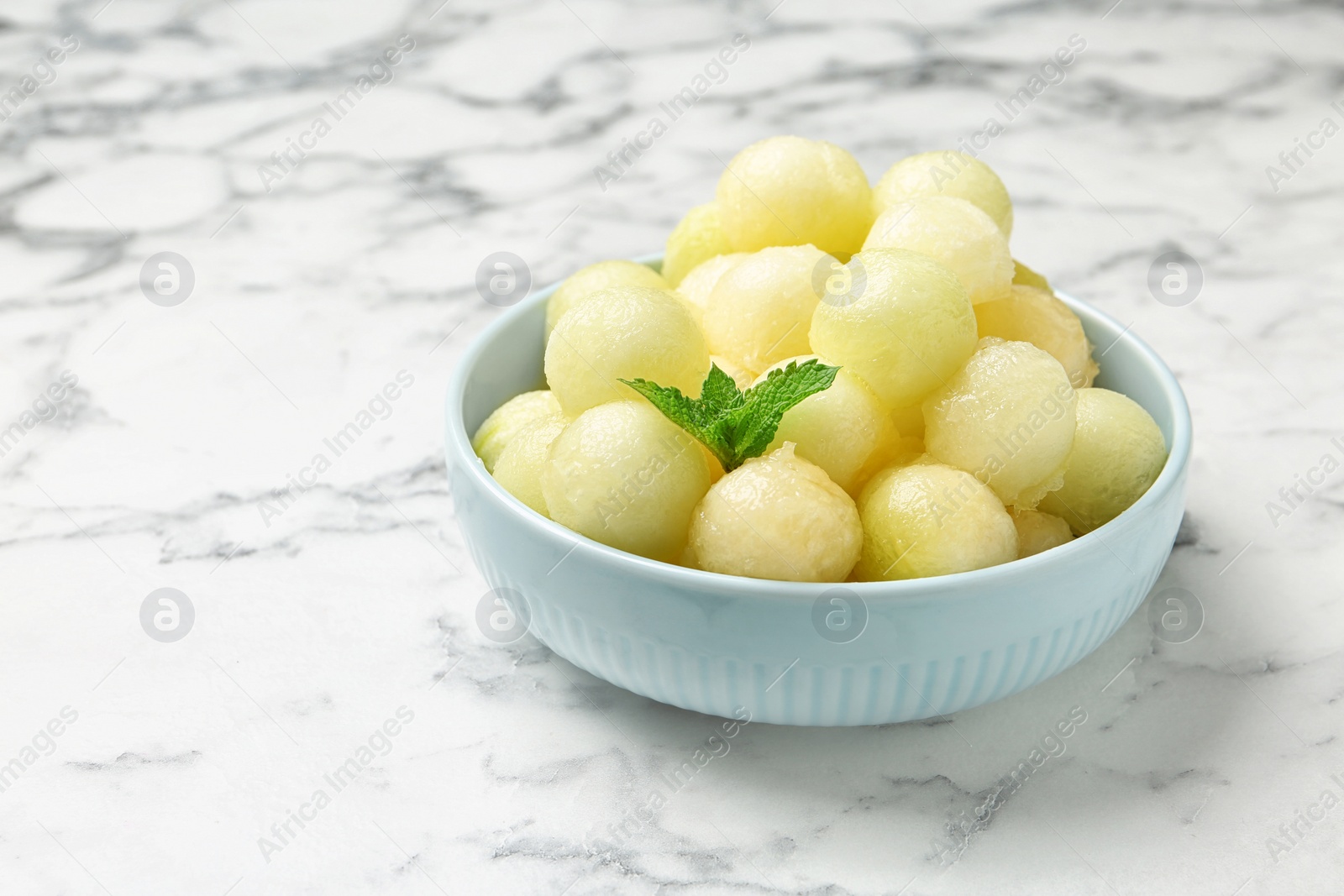 Photo of Plate of melon balls with mint on white marble table