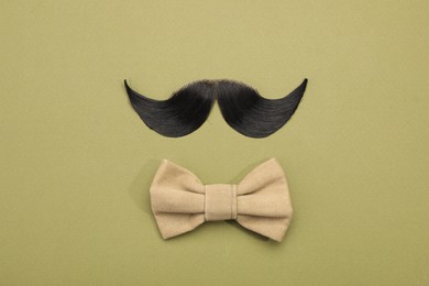 Photo of Artificial moustache and bow tie on khaki background, top view