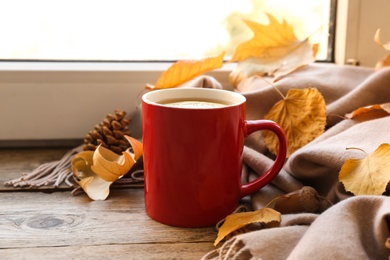 Photo of Cup of hot drink, scarf and autumn leaves on windowsill. Cozy atmosphere