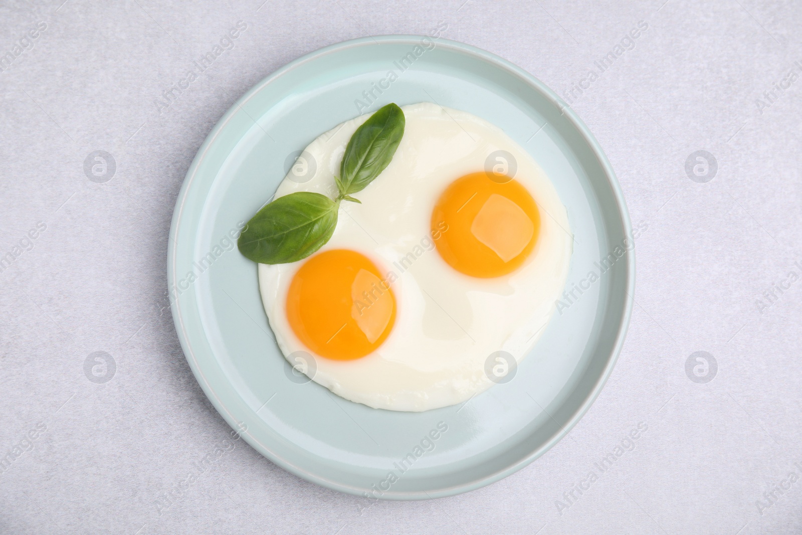 Photo of Tasty fried eggs with basil in plate on white table, top view