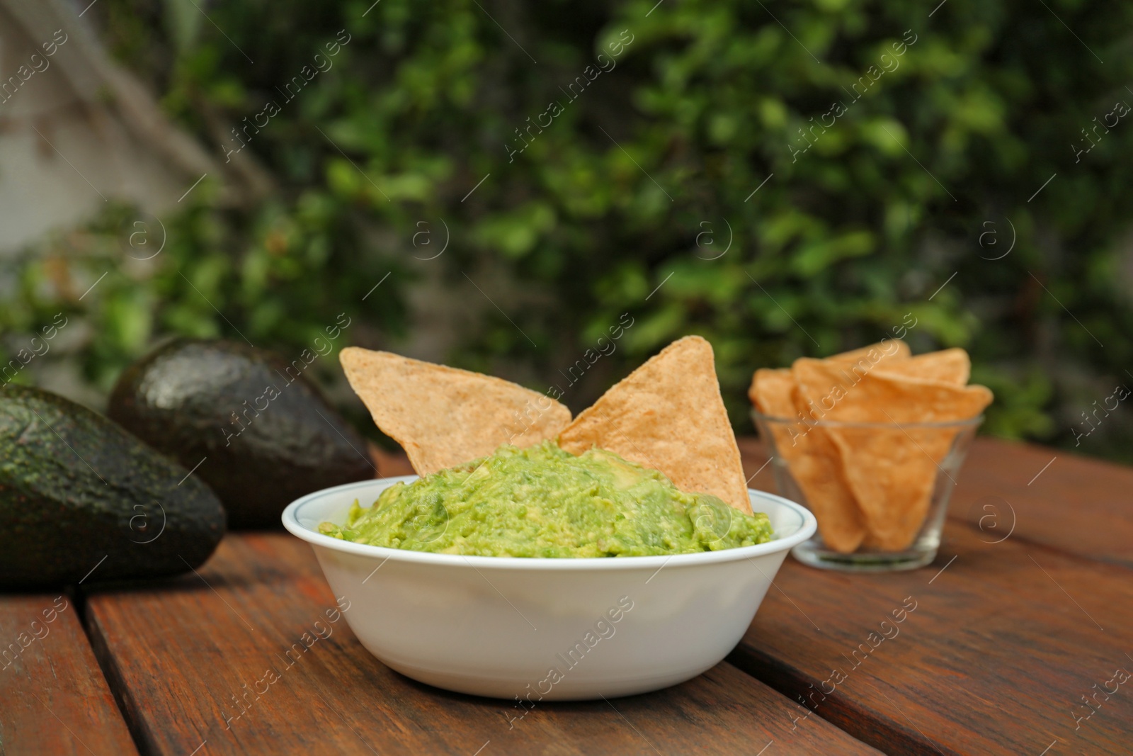Photo of Delicious guacamole, avocado and nachos on wooden table outdoors