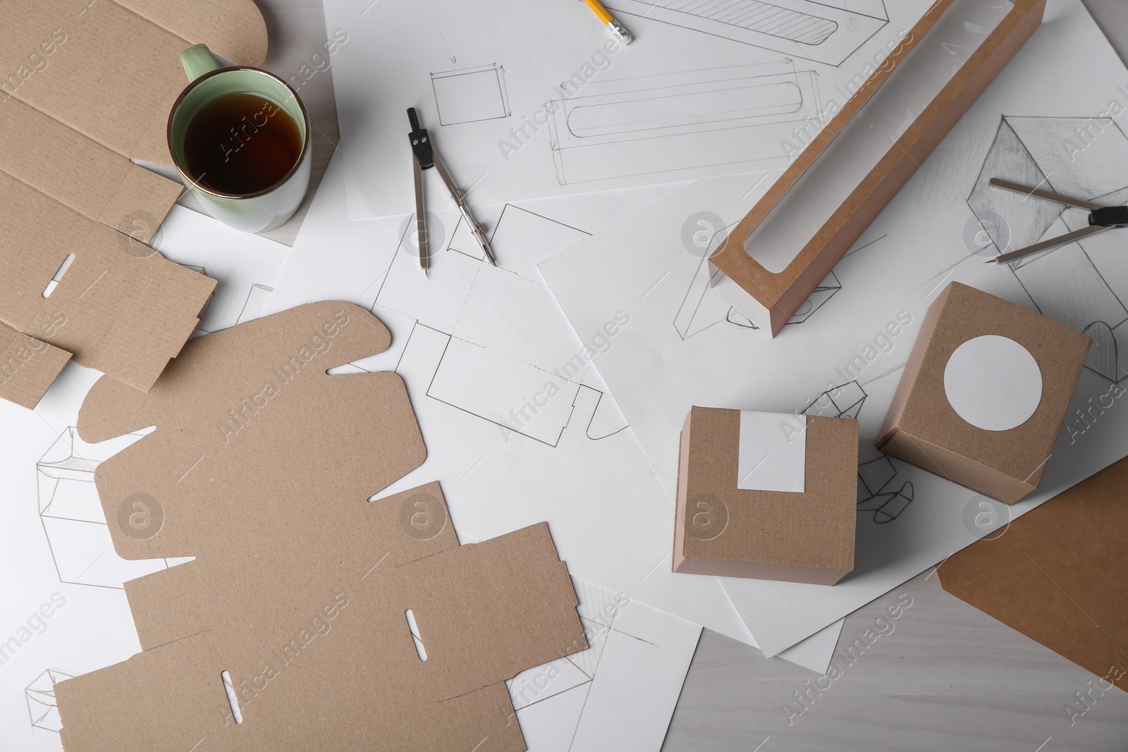 Photo of Creating packaging design. Drawings, boxes, coffee and stationery on light wooden table, flat lay