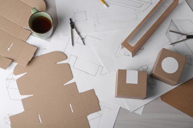 Creating packaging design. Drawings, boxes, coffee and stationery on light wooden table, flat lay