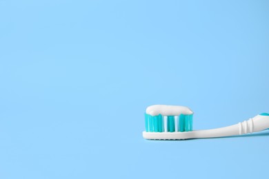 Photo of Brush with toothpaste on light blue background, space for text